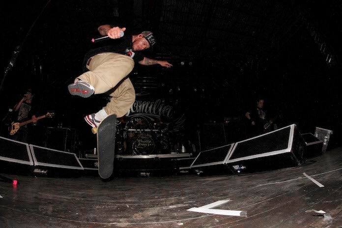 Chorão saltando de skate no palco durante um show, microfone na mão, com a banda ao fundo.